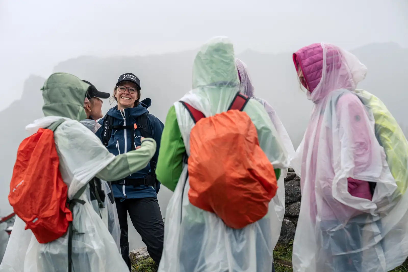 Achtsamkeitswanderung im Kufsteinerland MICE Ladies gehen in Regenponchos über eine neblige Almwiese
